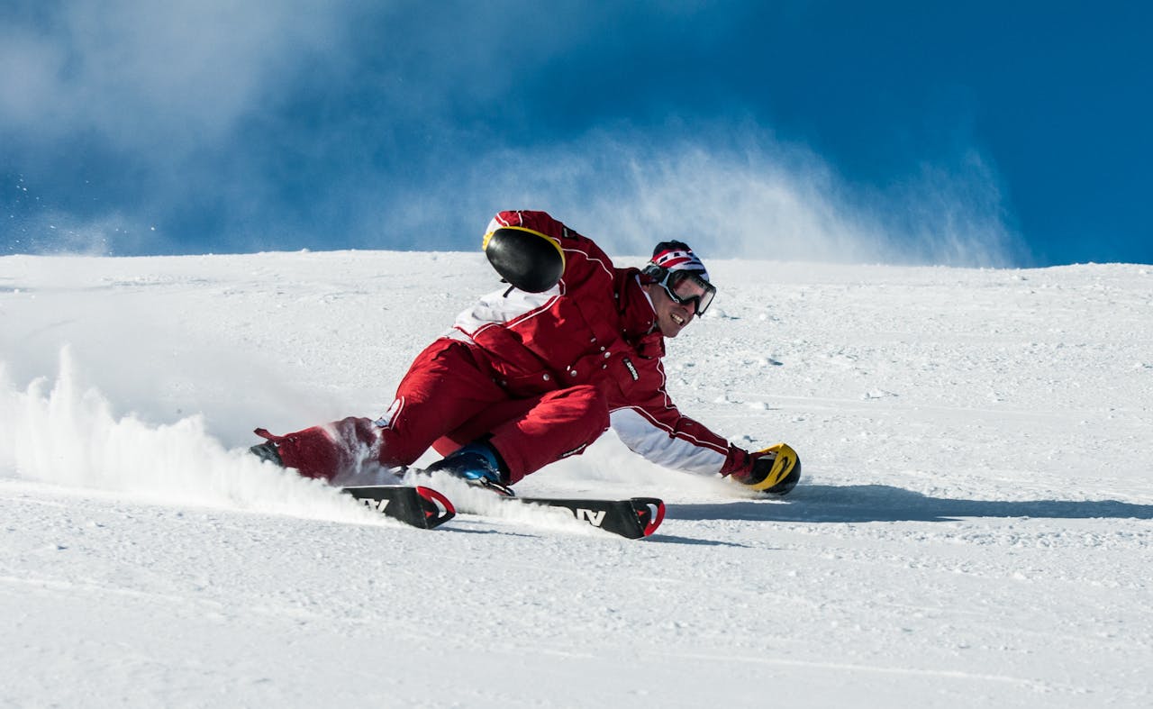 A skier in vibrant red gear skillfully navigates a snowy slope on a sunny day.